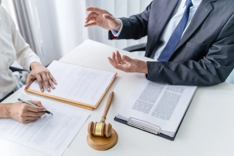 An adviser gesturing over a signed contract while a client writes
