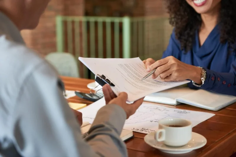 A client signing a document at a table while an adviser looks on, coffee cup alongside