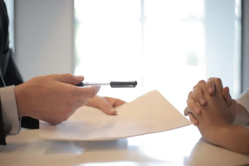One person handing a pen and document across a desk to another