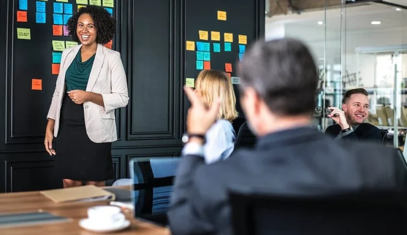 A trainer presenting to colleagues in a meeting room with sticky notes on the wall
